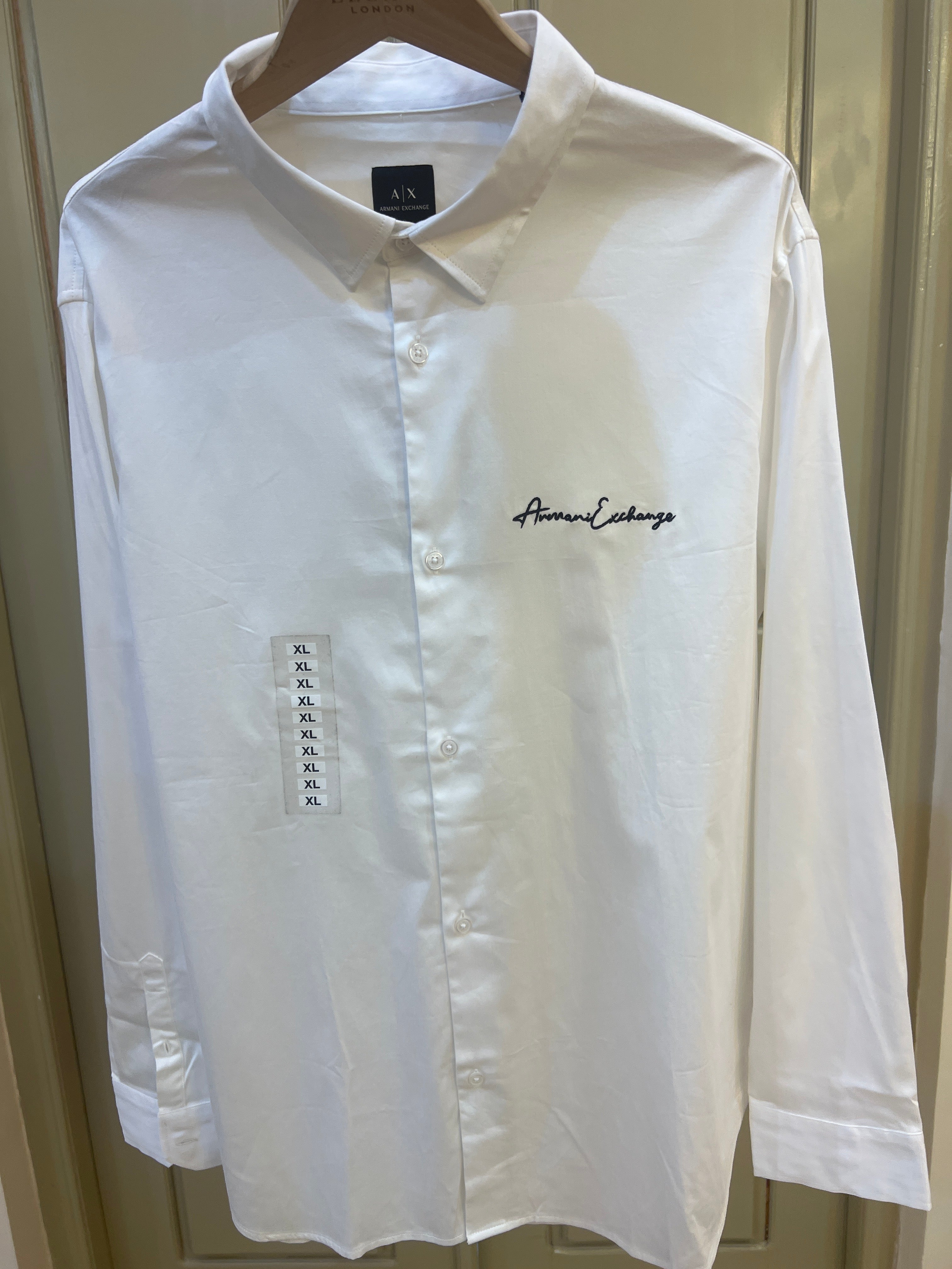 White long-sleeve Armani Exchange button-up shirt features a prominent cursive logo embroidered on the chest