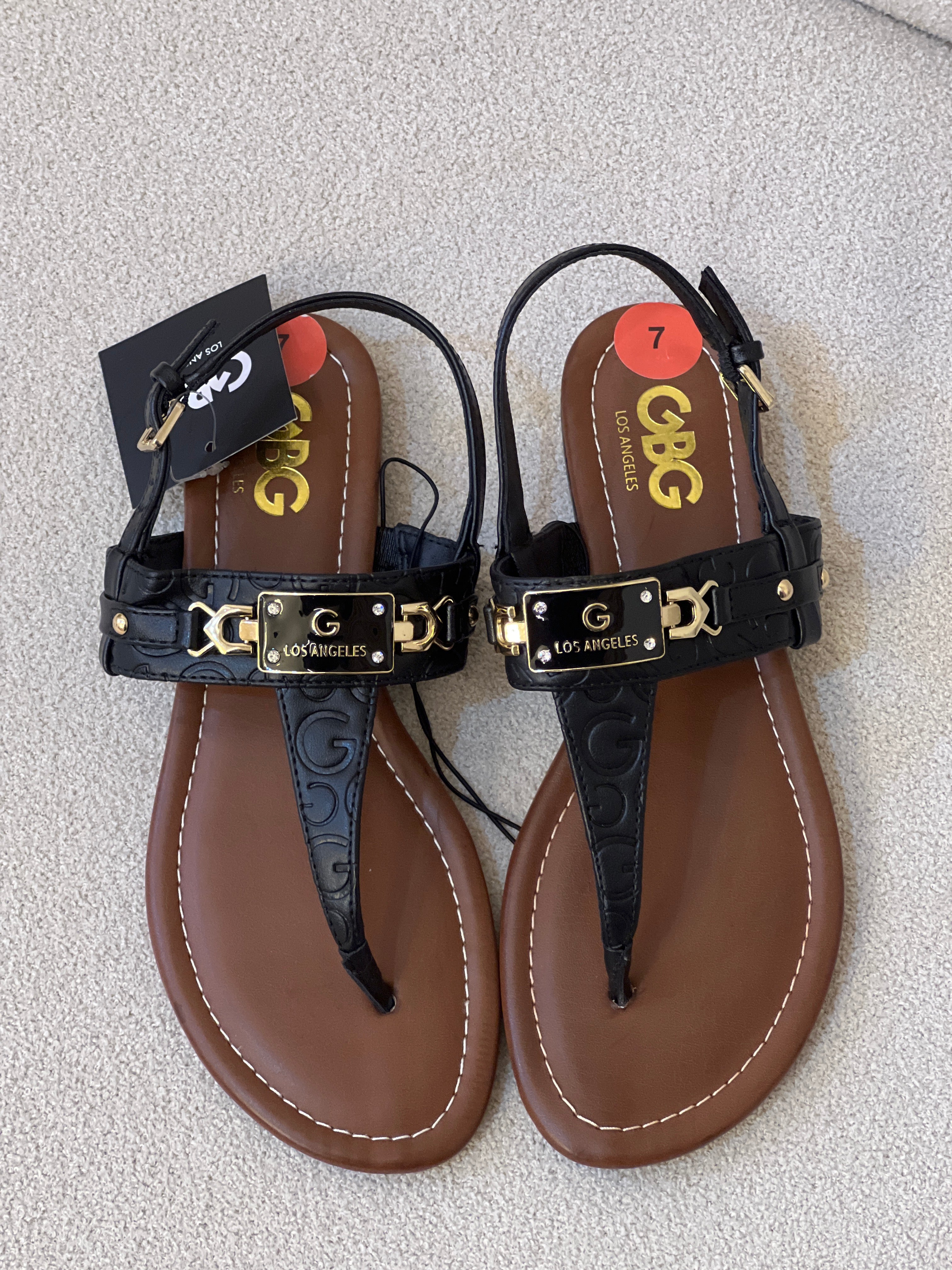 Women's GBG Los Angeles thong sandals, featuring a black strappy design with gold "G" hardware detailing