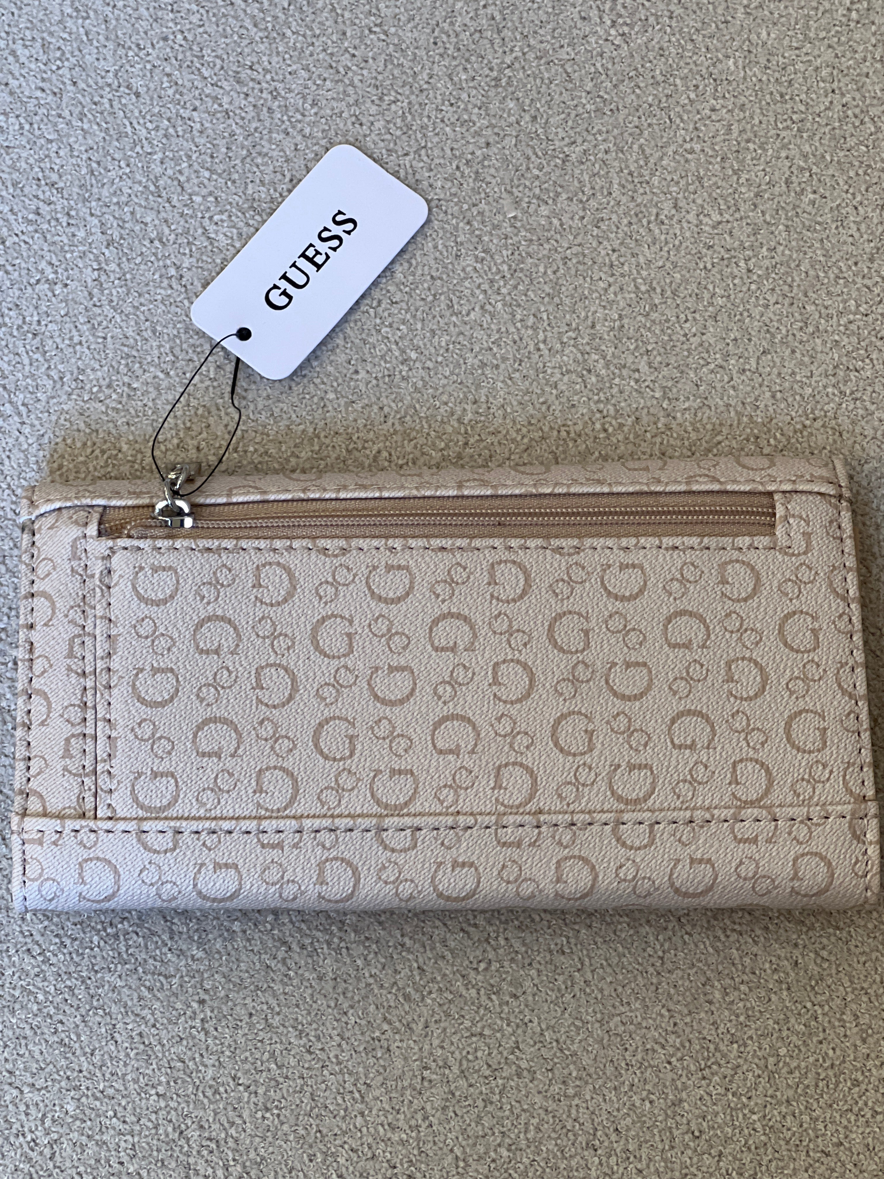 Beige Guess monogram clutch wallet features a silver-tone logo emblem on the front flap