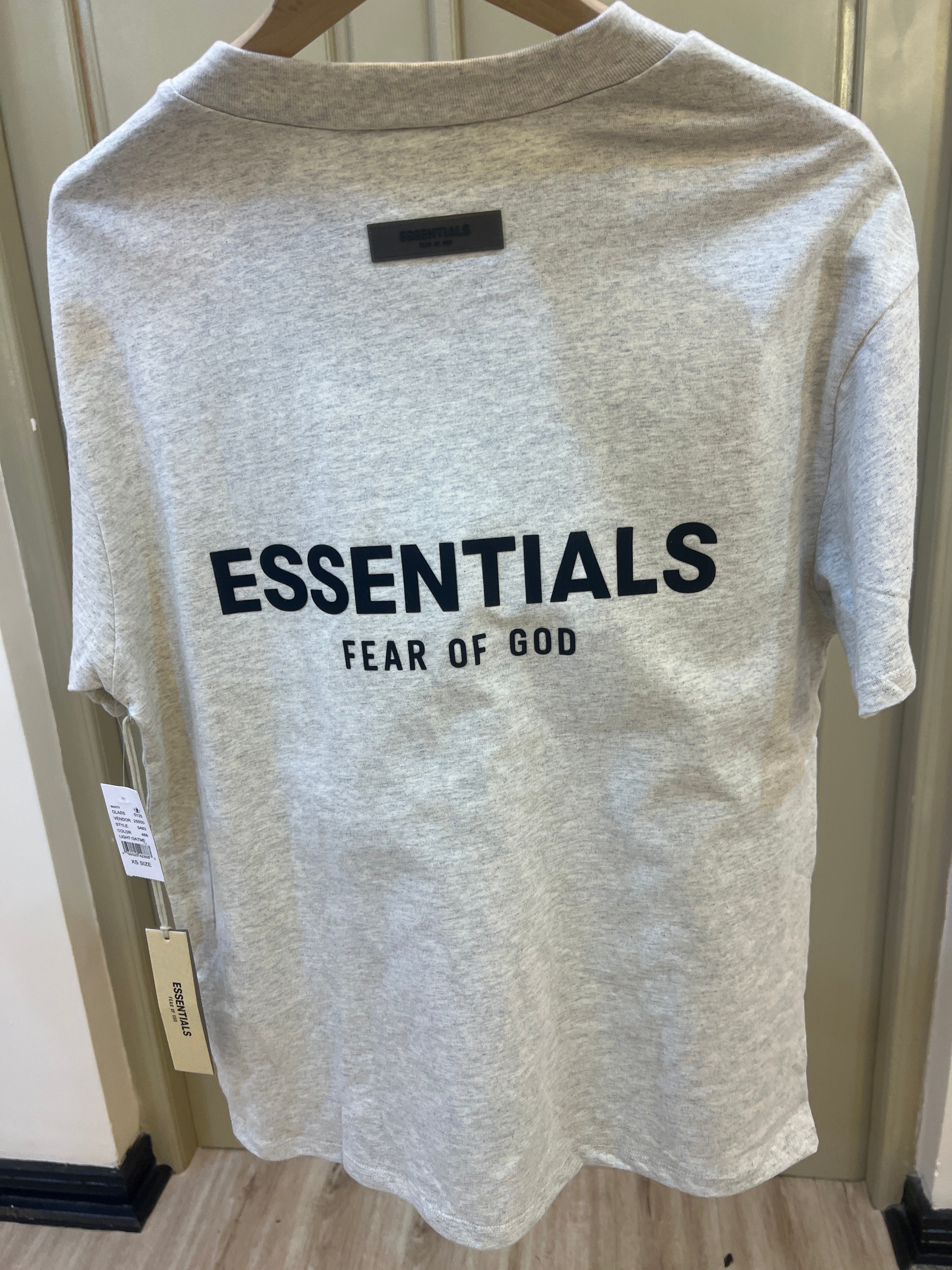 Fear of God Essentials T-shirt features a light oatmeal heather fabric and a contrasting black logo on the chest