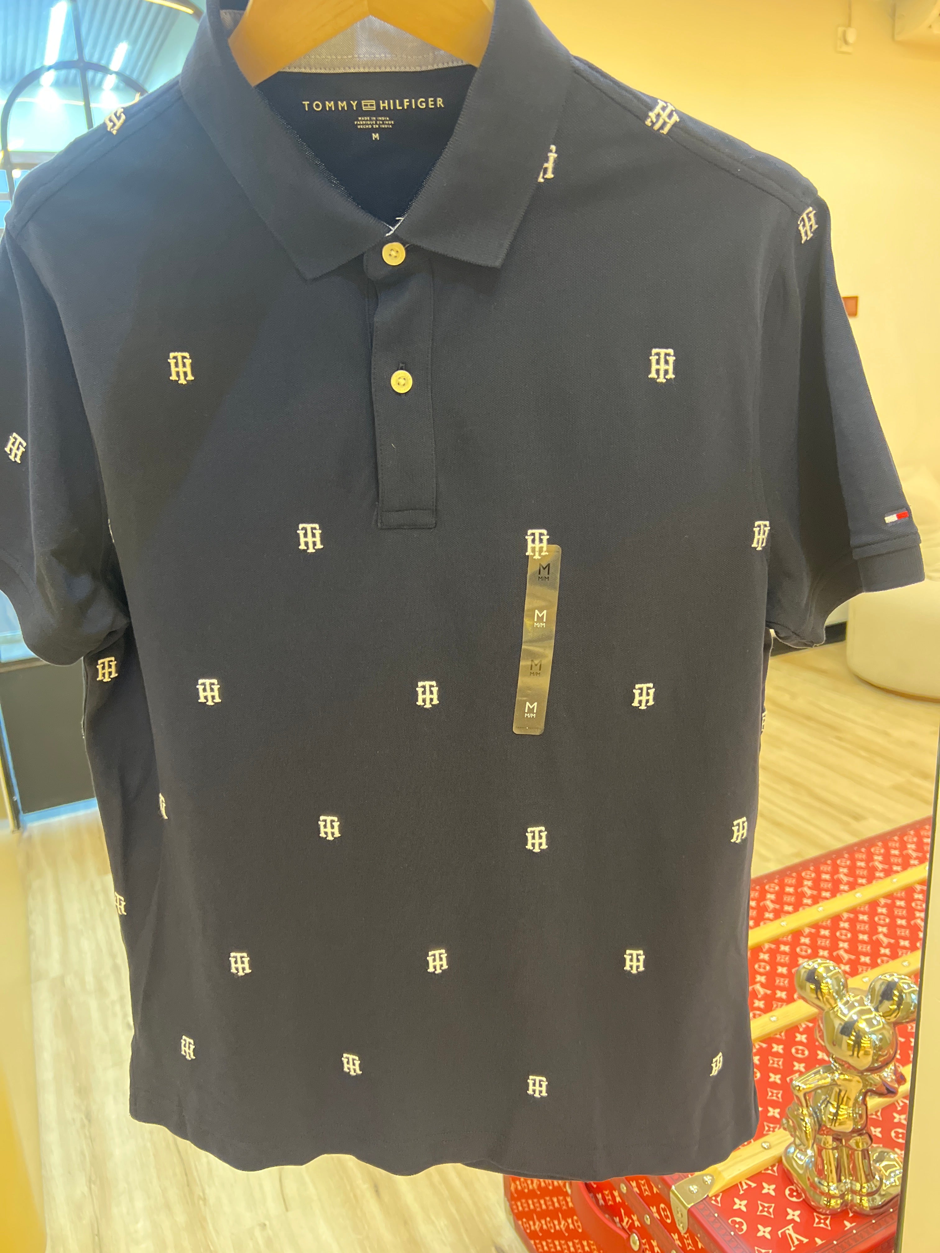 Navy blue Tommy Hilfiger men's polo shirt featuring a small embroidered logo pattern across the fabric