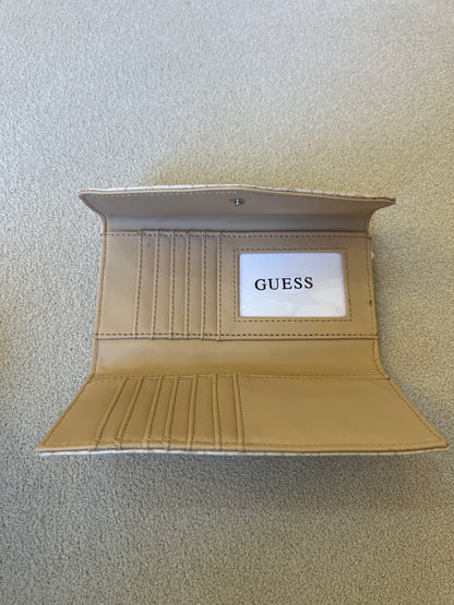 Beige Guess monogram clutch wallet features a silver-tone logo emblem on the front flap