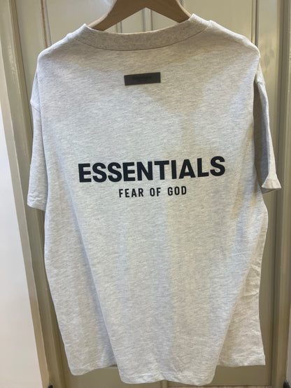 Fear of God Essentials t-shirt is rendered in a light oatmeal heather color and features a prominent branded logo on the chest