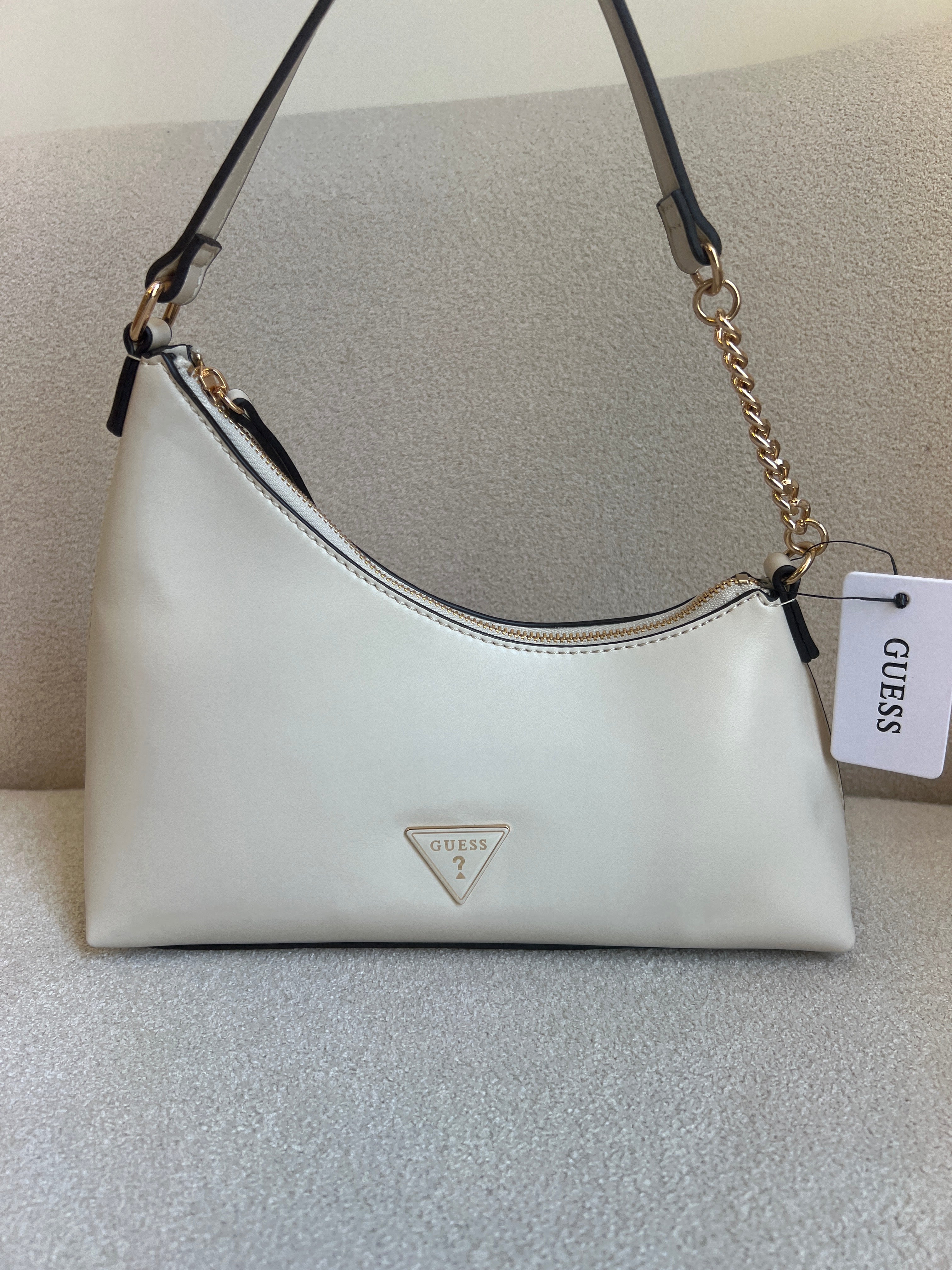 Guess Noelle top zip shoulder bag features a sleek white faux leather exterior with a distinctive triangular logo plaque