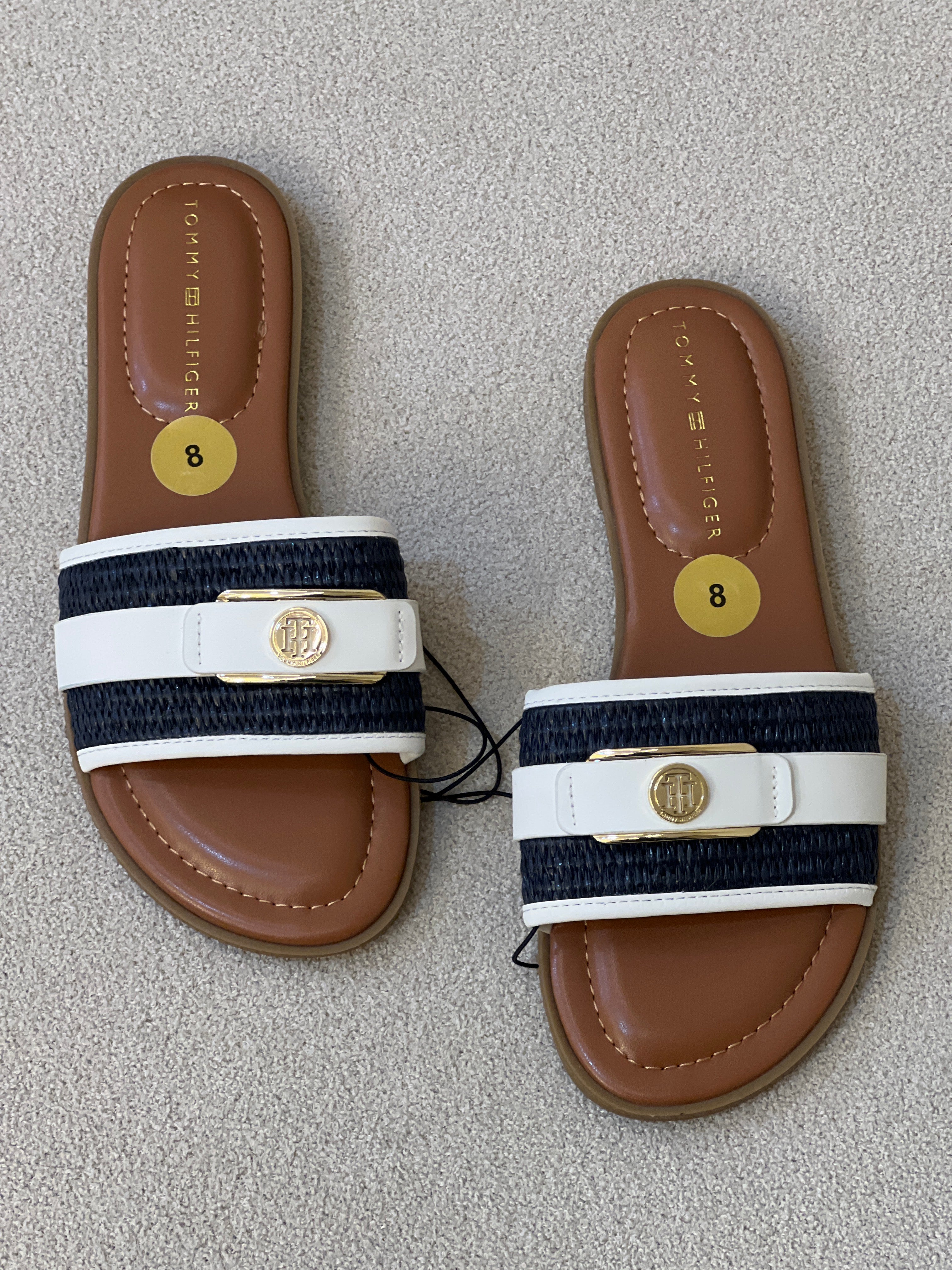 Tommy Hilfiger sandals feature a white strap with gold branding, a navy woven base, and a size 8 label