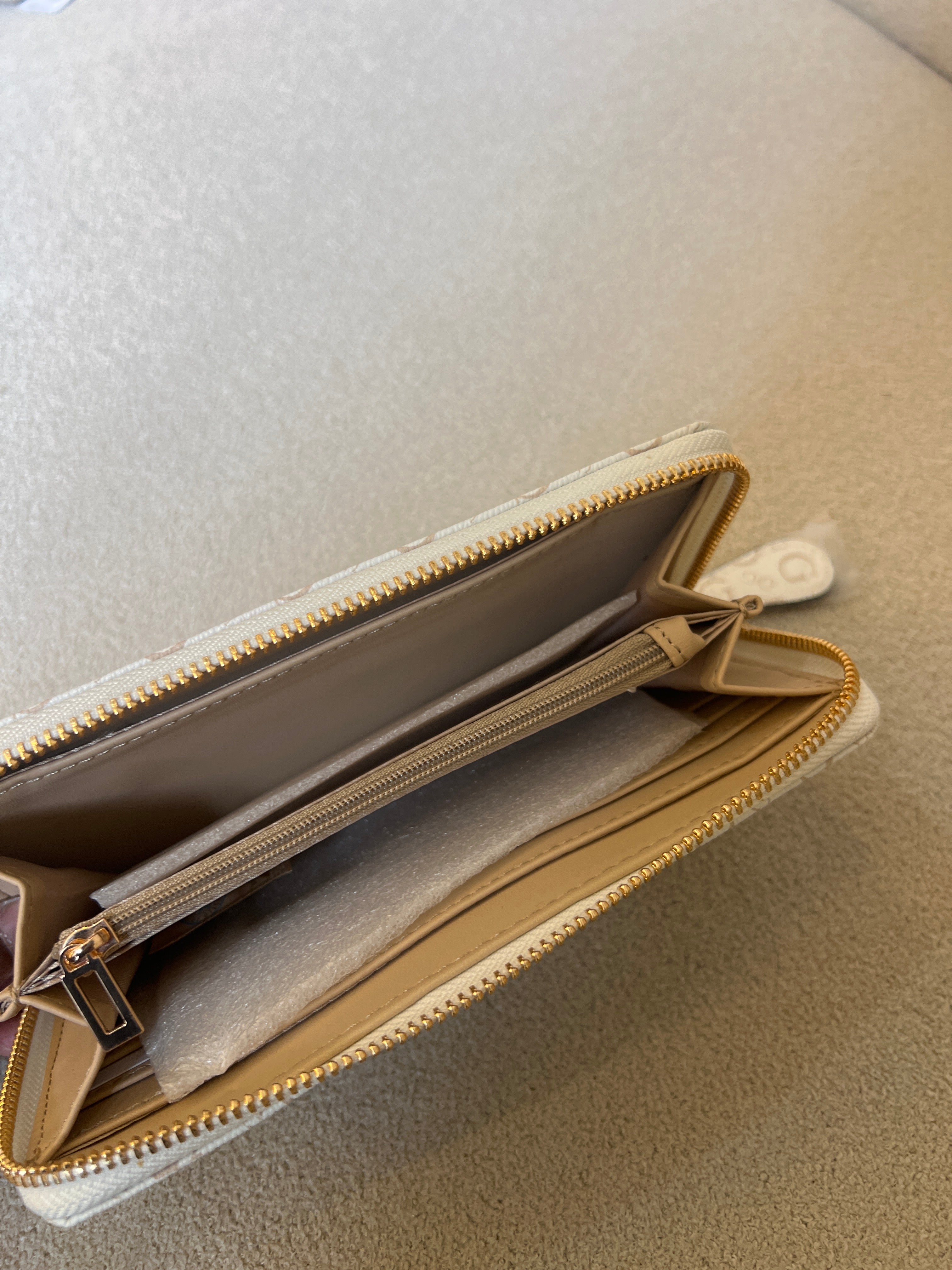 Guess Isabella zip-around wallet features a white printed design with a tan center strap and a prominent gold logo plaque