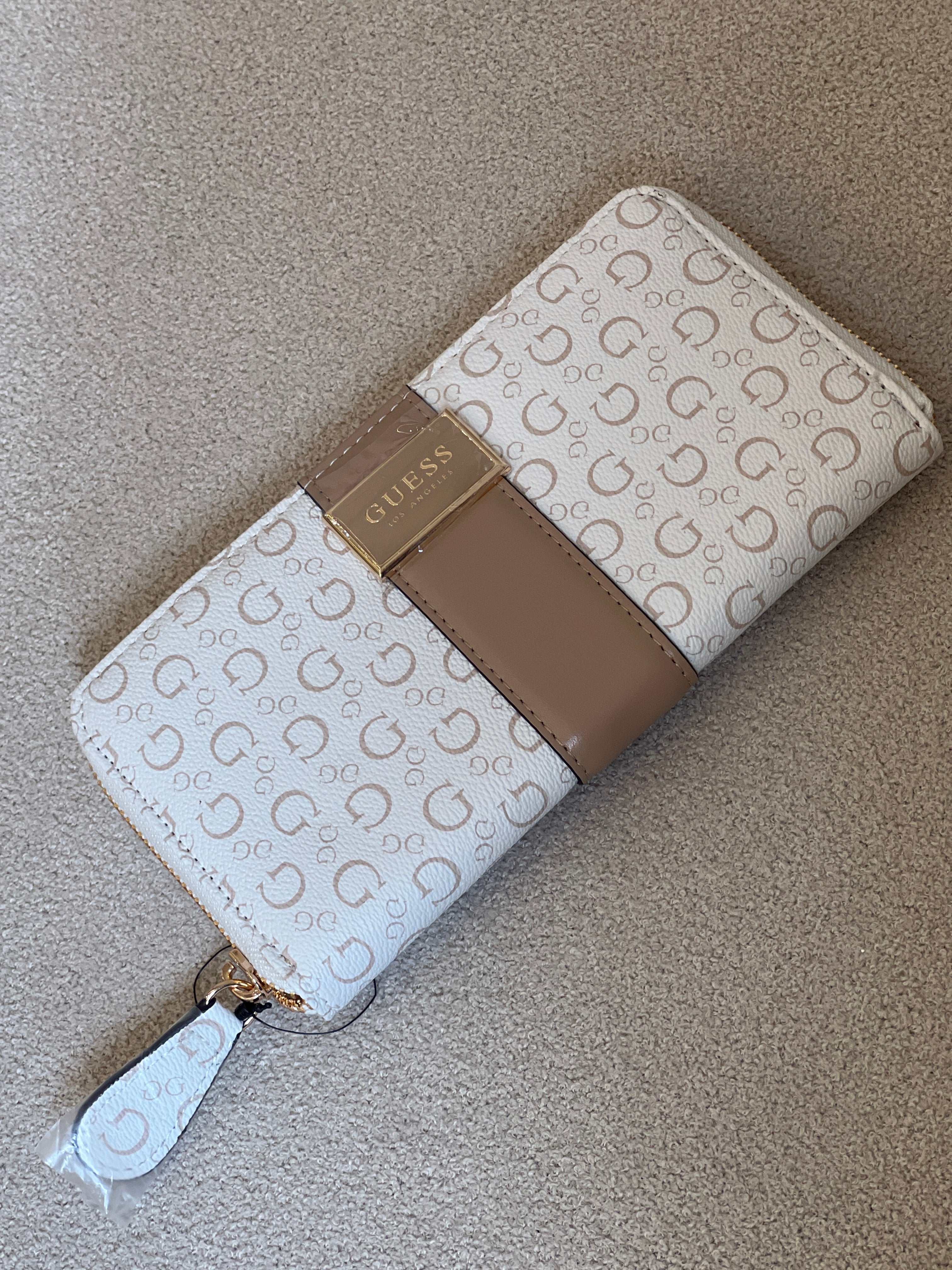 Guess Isabella zip-around wallet features a white printed design with a tan center strap and a prominent gold logo plaque