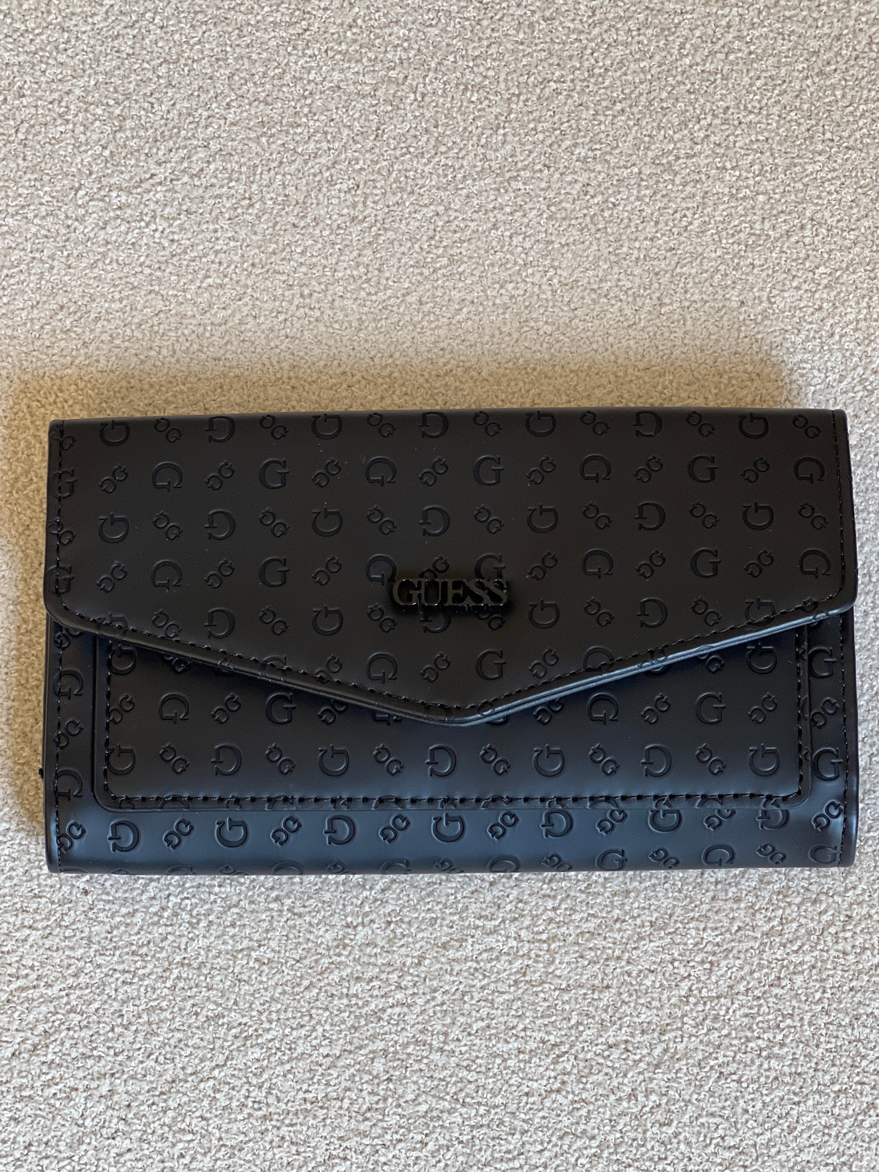 Guess monogram wallet features a distinctive embossed logo pattern and a snap closure