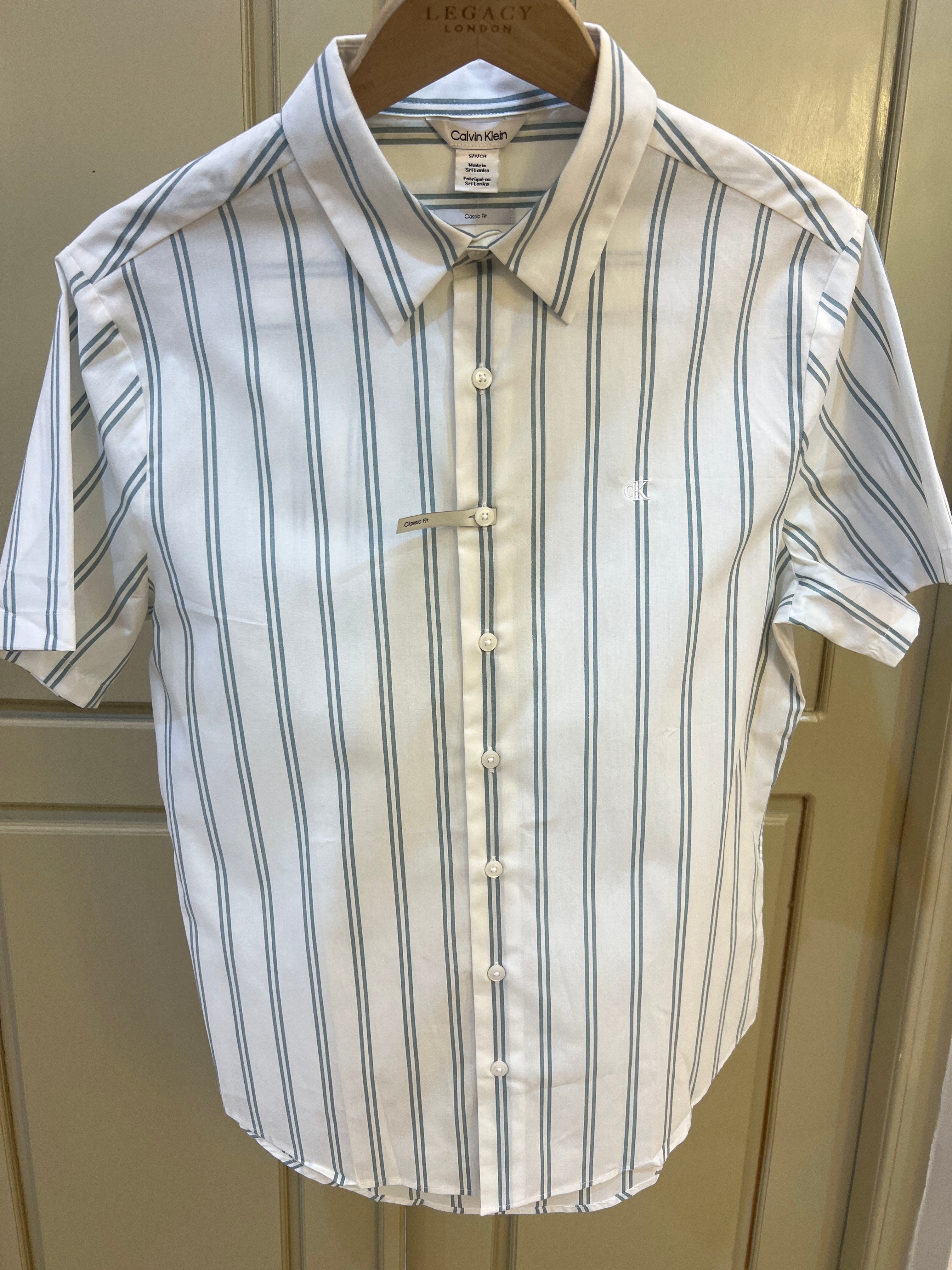 Calvin Klein short-sleeve button-down shirt features a crisp white fabric adorned with thin grey vertical stripes and a small embroidered logo on the chest