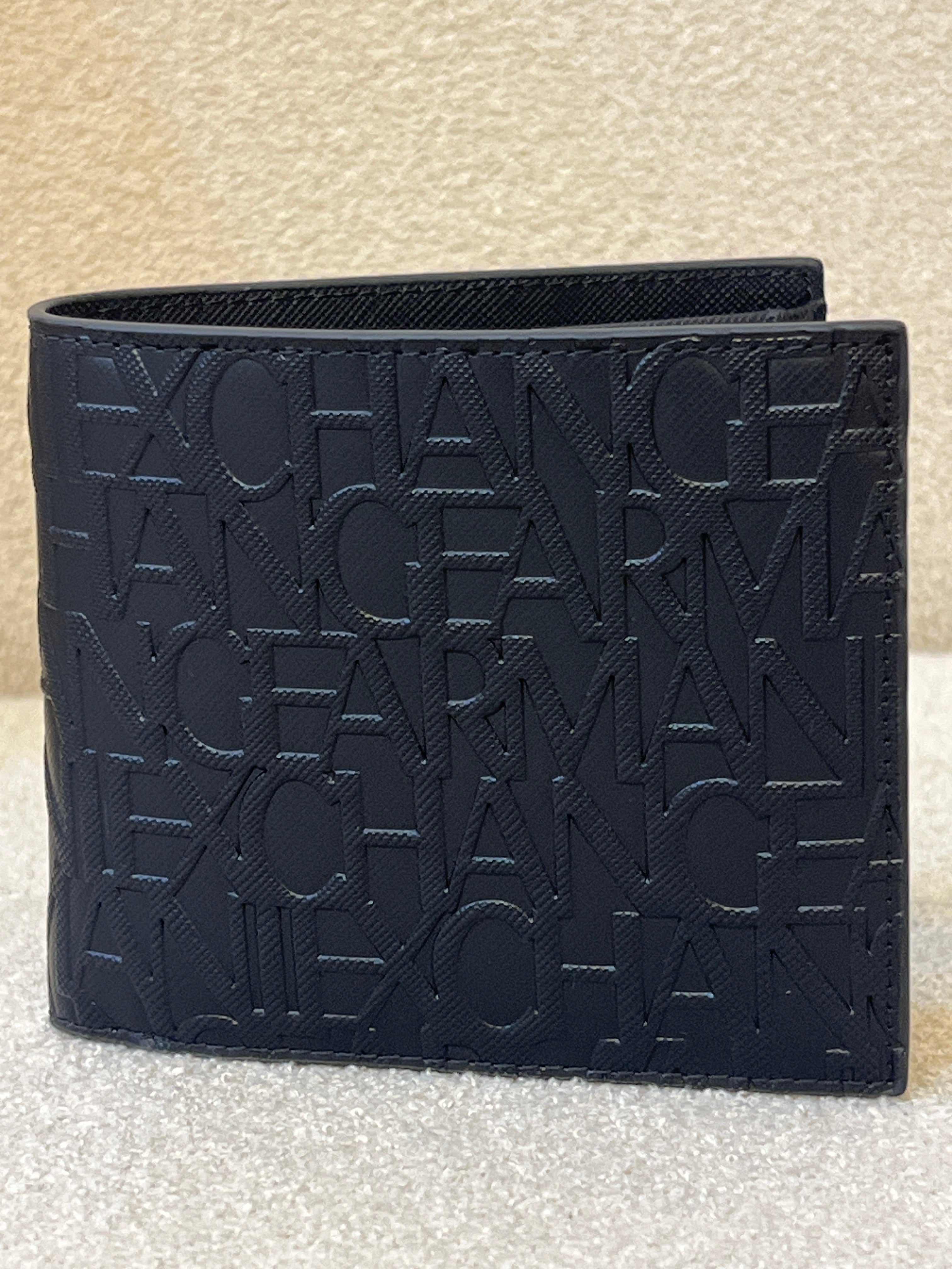 Armani Exchange bifold wallet, likely model 958098_CC838, featuring an all-over embossed logo design in black