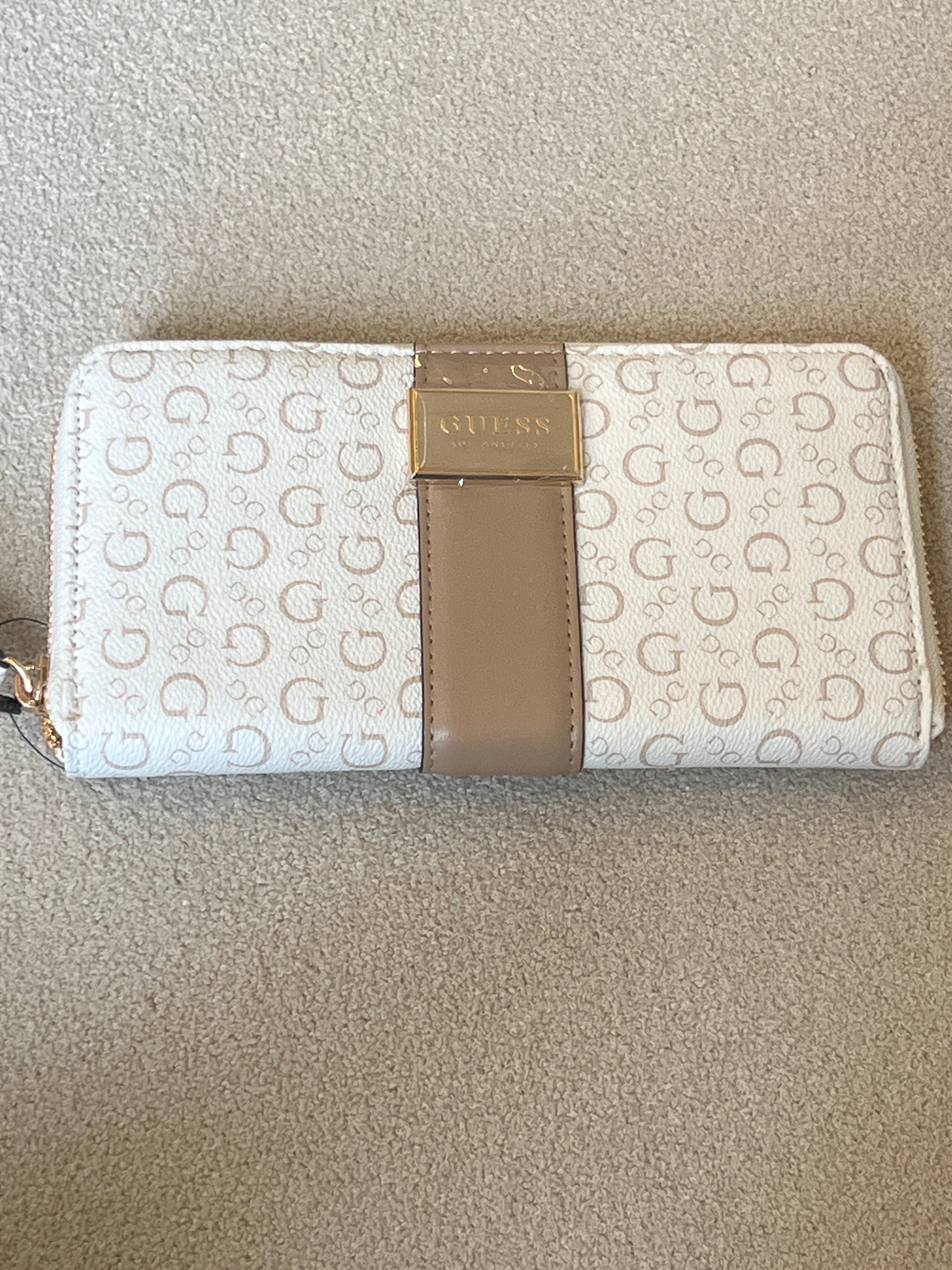 Guess Isabella zip-around wallet features a white printed design with a tan center strap and a prominent gold logo plaque